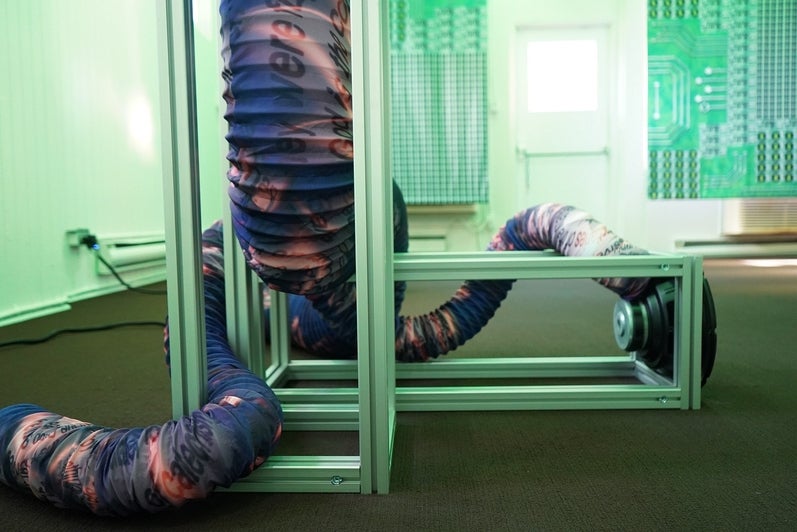 Artwork with expandable tubing printed with text and patterns, loops through a metal frame sitting on the floor.