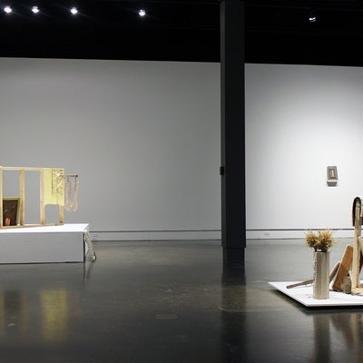 View of an art gallery installation with two assemblages on the floor.