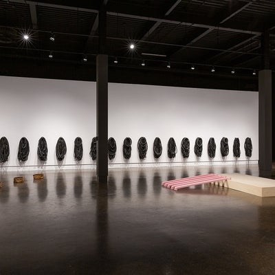 Artwork in a gallery. On walls, multiple groups of bike tubes. On floor, series of large round paperbags and pink cast eaverstro