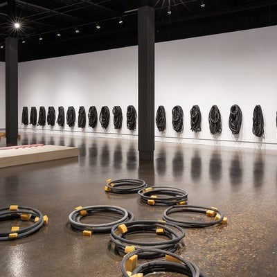 Artwork in a gallery. On walls, multiple groups of bike tubes. On floor, piles of circular black plaster casts with yellow foam