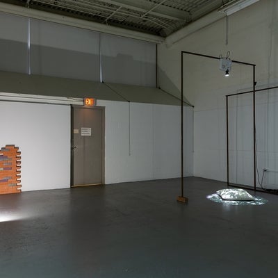 Industrial space with art installation. Brick-like objects are piled against a wall and a digital projectors lights an object on
