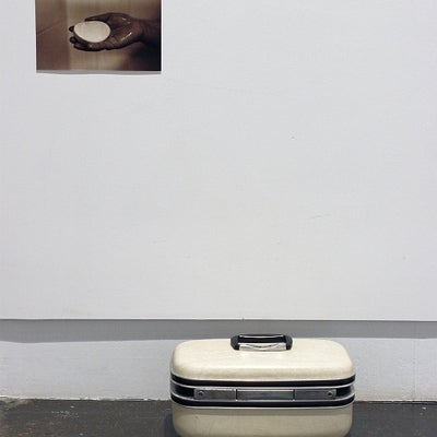 Art installation of a vintage makeup case on the floor with a sepia photograph hanging above showing a hand with a bar of soap