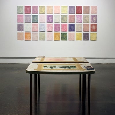Art gallery exhibiton with 44 multi-coloured prints of a graduation photo arrange in a grid pattern and 2 small tables