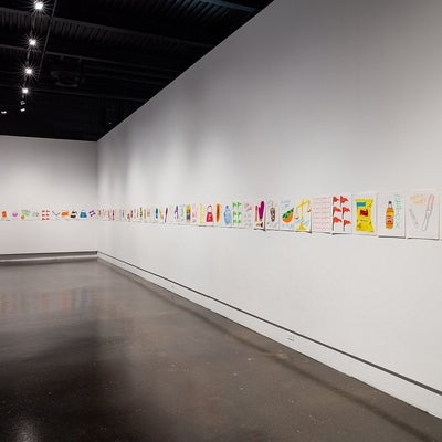 Art exhibit with a series of colourful drawings of objects and text all pinned to the wall in a row.