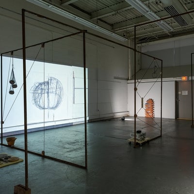 Dark, industrial space with art installation. Projectors light objects on the concrete floor and video of a drawing on the wall