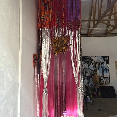 Fabric sculpture of silver and red ribbons hanging from floor to ceiling in a studio space.