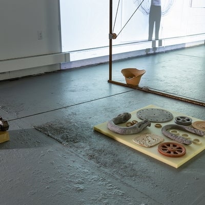 Industrial space with art installation. Ceramic objects of gears and pulleys sit on a concrete floor.