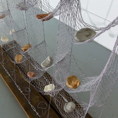 Artwork of suspended hammock-like net with sections holding rock-like ceramic objects.