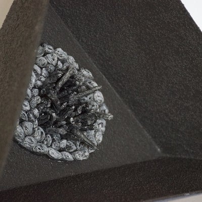 Close-up of a small, dark, pyramid form. One side is recessed with small irregular shapes protruding from the surface.