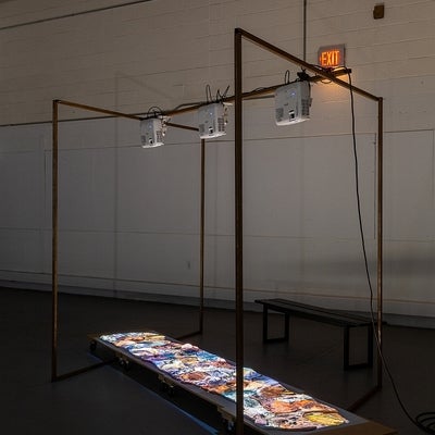 Industrial space with artwork. Projectors on metal frame display video of water flowing over rocks on ceramic shapes on floor