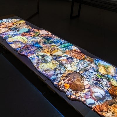 Video of water flowing over rocks is projected on ceramic shapes on floor