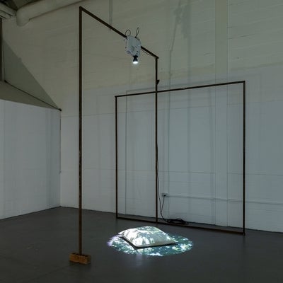Industrial space with artwork. Metal frame supports a digital projector shining the image of dappled sunlight on a floor pillow