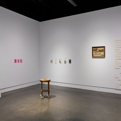 Art gallery installation of vintage ephemera, and marble topped table standing on bricks, white ceramic tiles, and a vintage landscape painting.