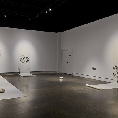 Art gallery installation of large scrolls with charcoal drawings of circular shapes hang on the wall and unroll onto the floor.