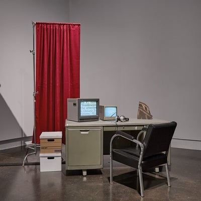 Videos run on two vintage televisions sitting on industrial office desk in front of  a privacy screen.
