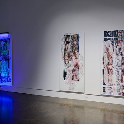 Art gallery installation of three large scale prints of distorted medical scans, one lit by ultraviolet light.