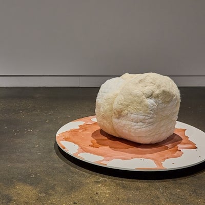 Large white and cream, spherical, fabric sculpture on a circular platform decorated with an oxidized stain.