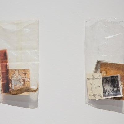 Two clear plastic bags containing old photos, ephemera and a lock of hair, hang on a wall.