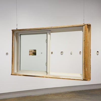 A salvaged house window hangs from the ceiling in front of a wall displaying a row of shells.