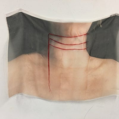 Colour photograph printed on sheer fabric depicting a person's neck and shoulders.  Red thread is embroidered in three lines across the neck with the remaining thread hanging down..