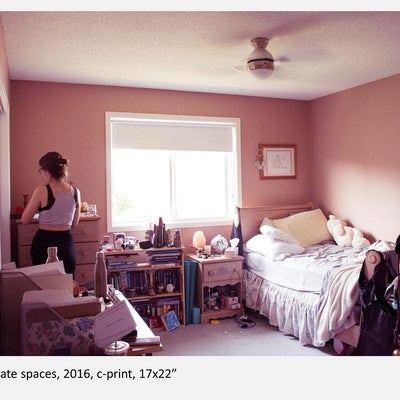 Warm-pink tinged photograph of person standing in a cluttered bedroom