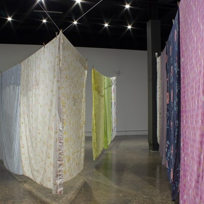 View of an art exhibition with multi-coloured and patterned bedsheets hung on what resemble clotheslines