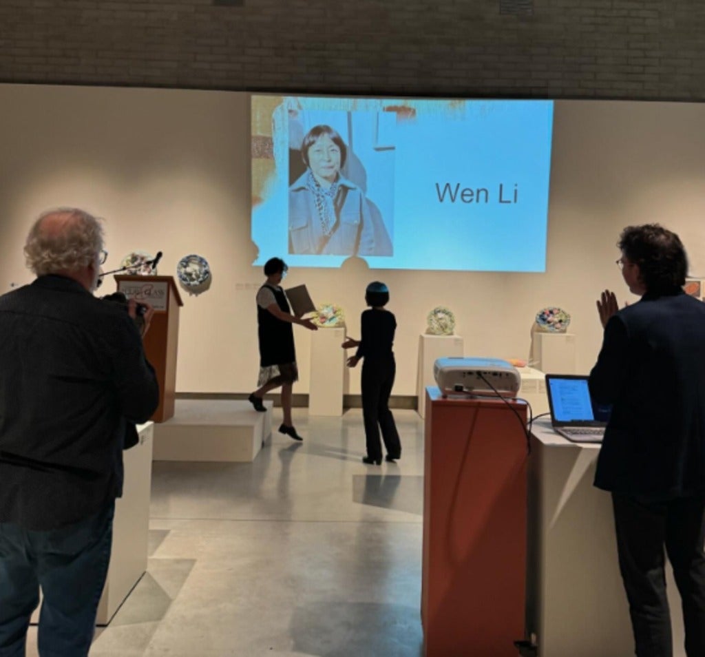 Several people applaud while Wen Li is presented with an award. 