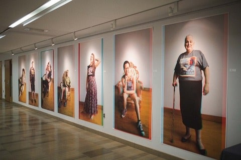 Hallway displaying wall-sized, 3D anaglyphic, full figure portrait photographs of trans people.