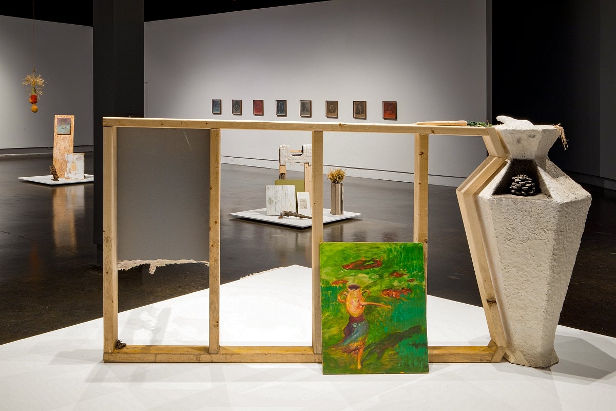 View, through a wooden frame, of an art gallery installation with coloured drawing on the wall and several assemblages on floor