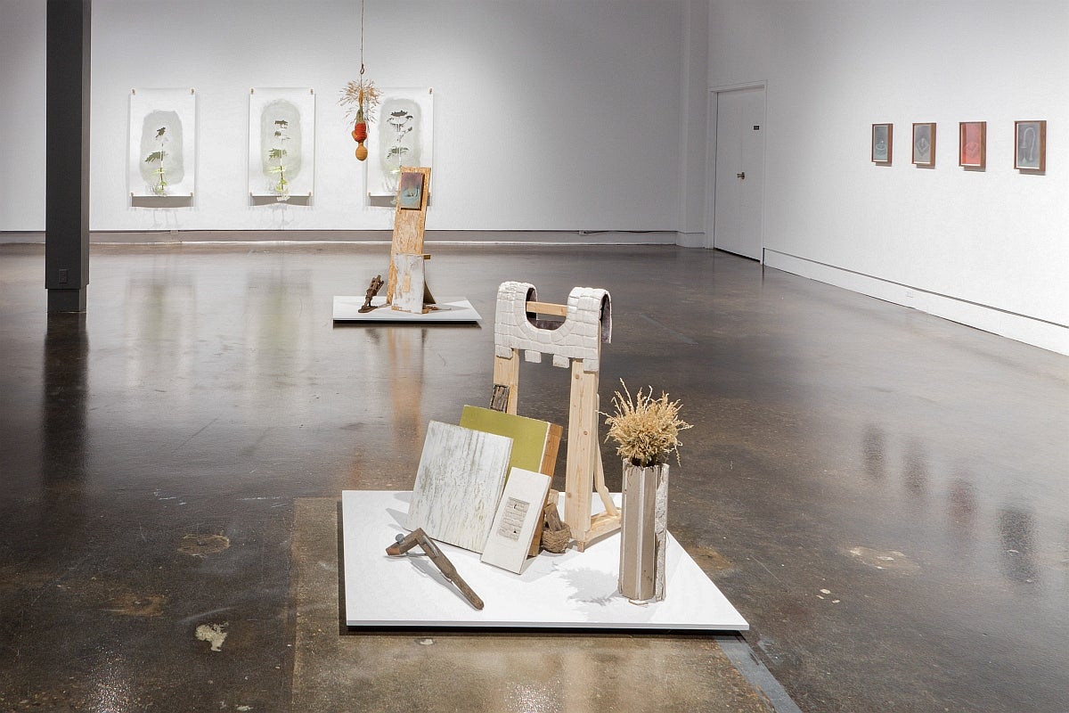 View of an art gallery installation with coloured graphite drawing on the wall and several assemblages on the floor.