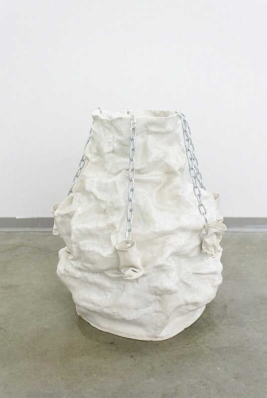Large ceramic sculpture resembling a filled white cotton sack, with four smaller "bags" hung by chains to the top lip.