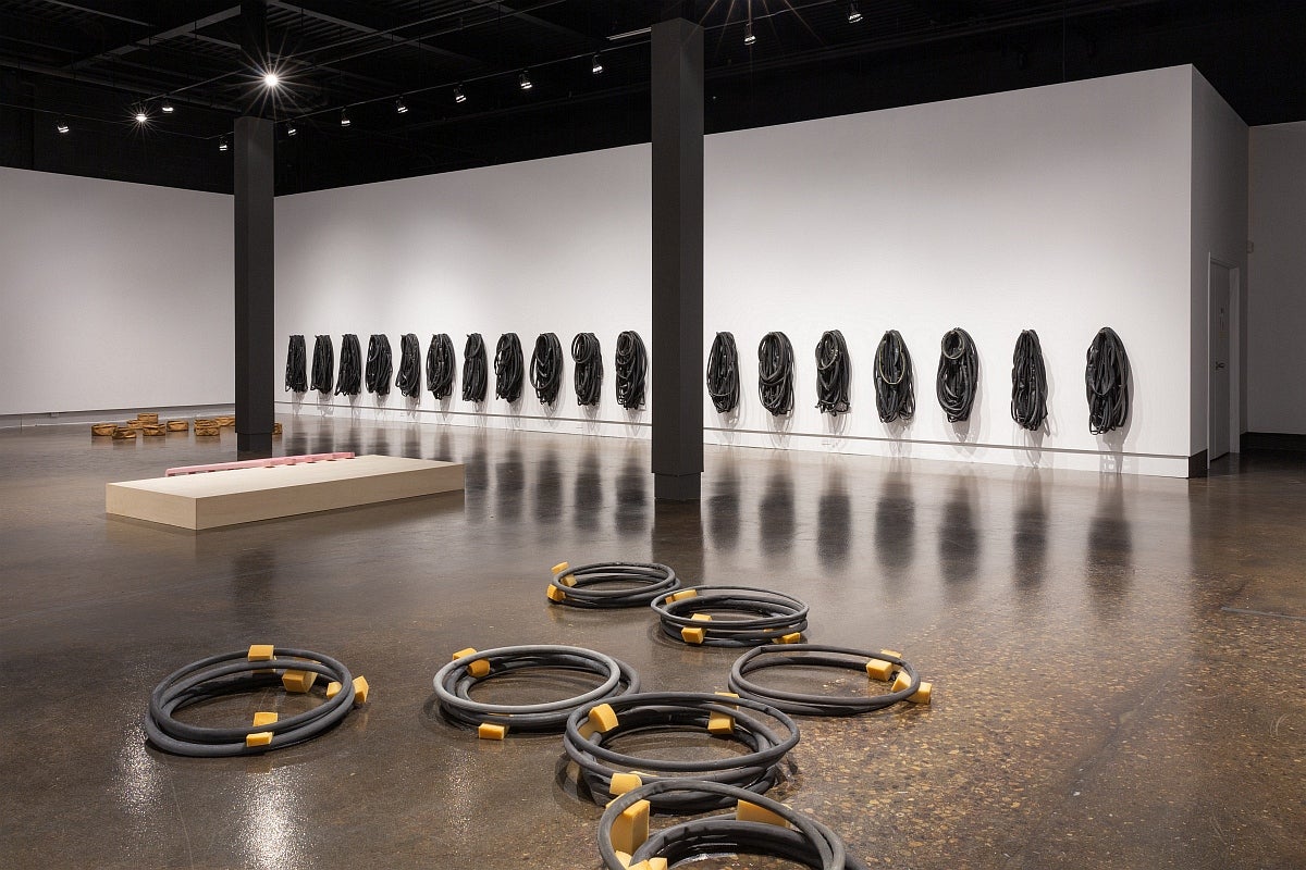 Artwork in a gallery. On walls, multiple groups of bike tubes. On floor, piles of circular black plaster casts with yellow foam