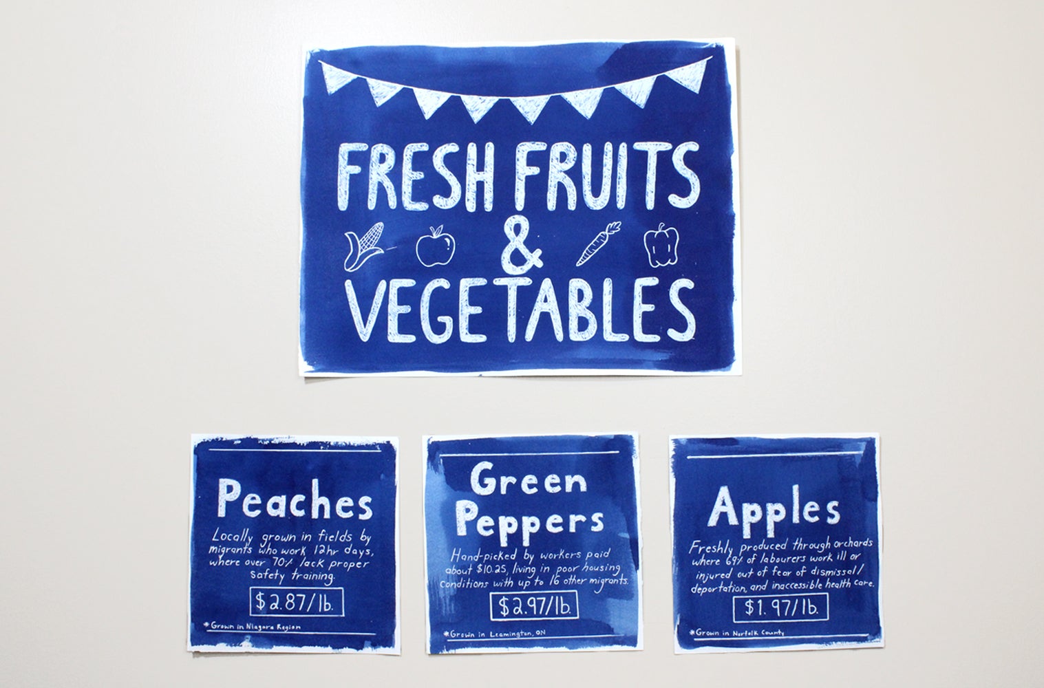 Artwork in blue and white, advertising signs for fruit and vegetables describing working conditions of farm labour