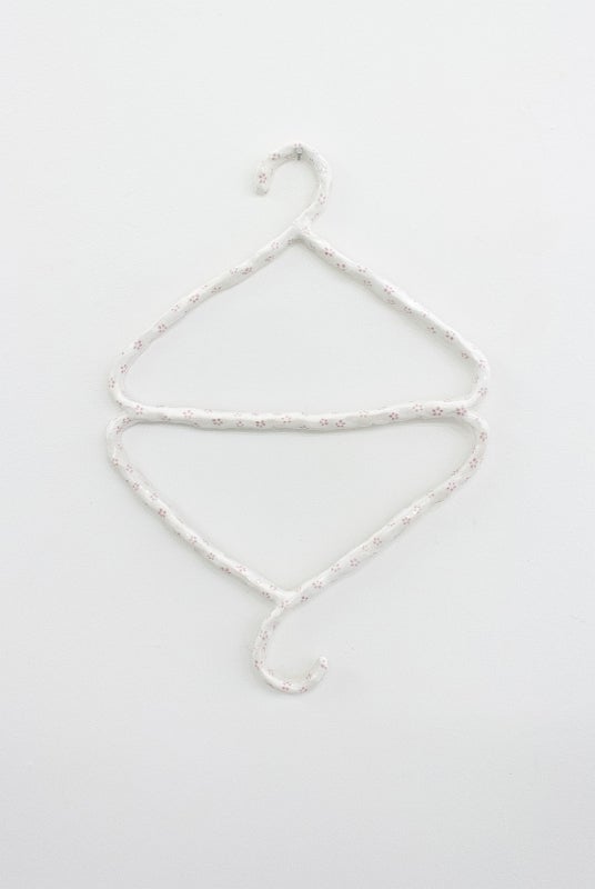 White ceramic sculpture in the shape two clothes hangers joined at the bottom edge so one hangs upside down.