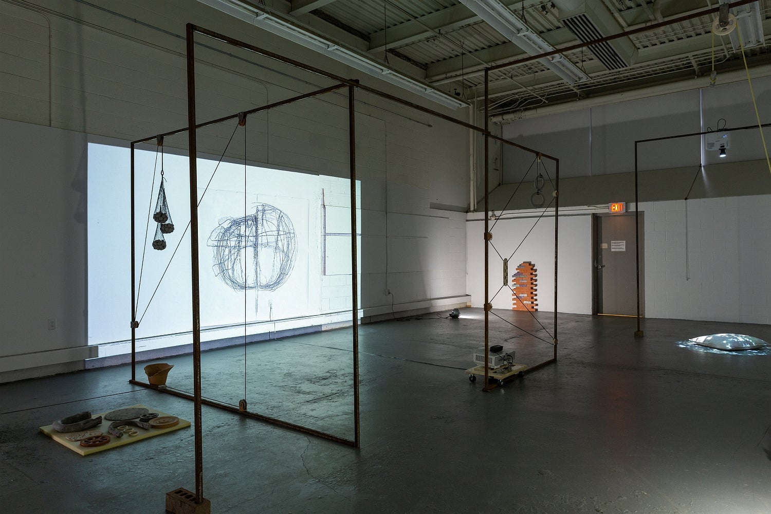 Dark, industrial space with art installation. Projectors light objects on the concrete floor and video of a drawing on the wall