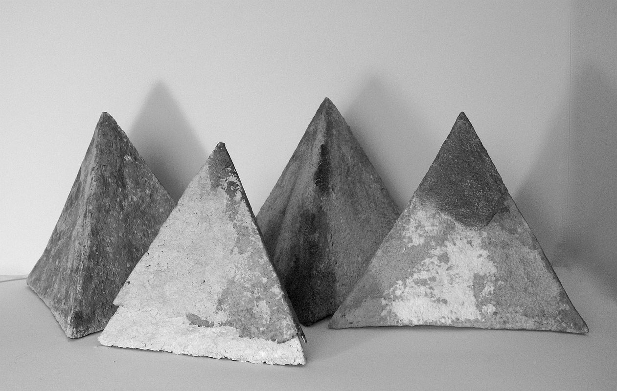 Black and white photo of four small pyramids with rough, irregular surfaces.