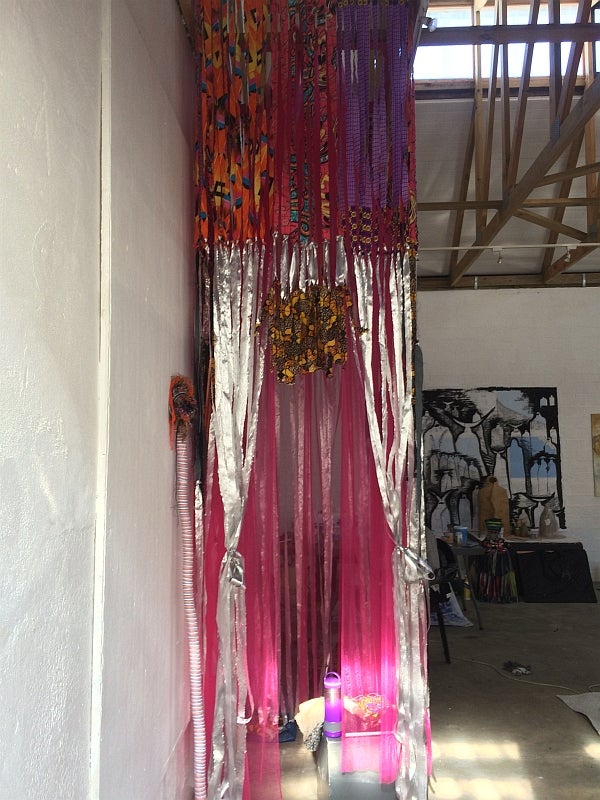 Fabric sculpture of silver and red ribbons hanging from floor to ceiling in a studio space.