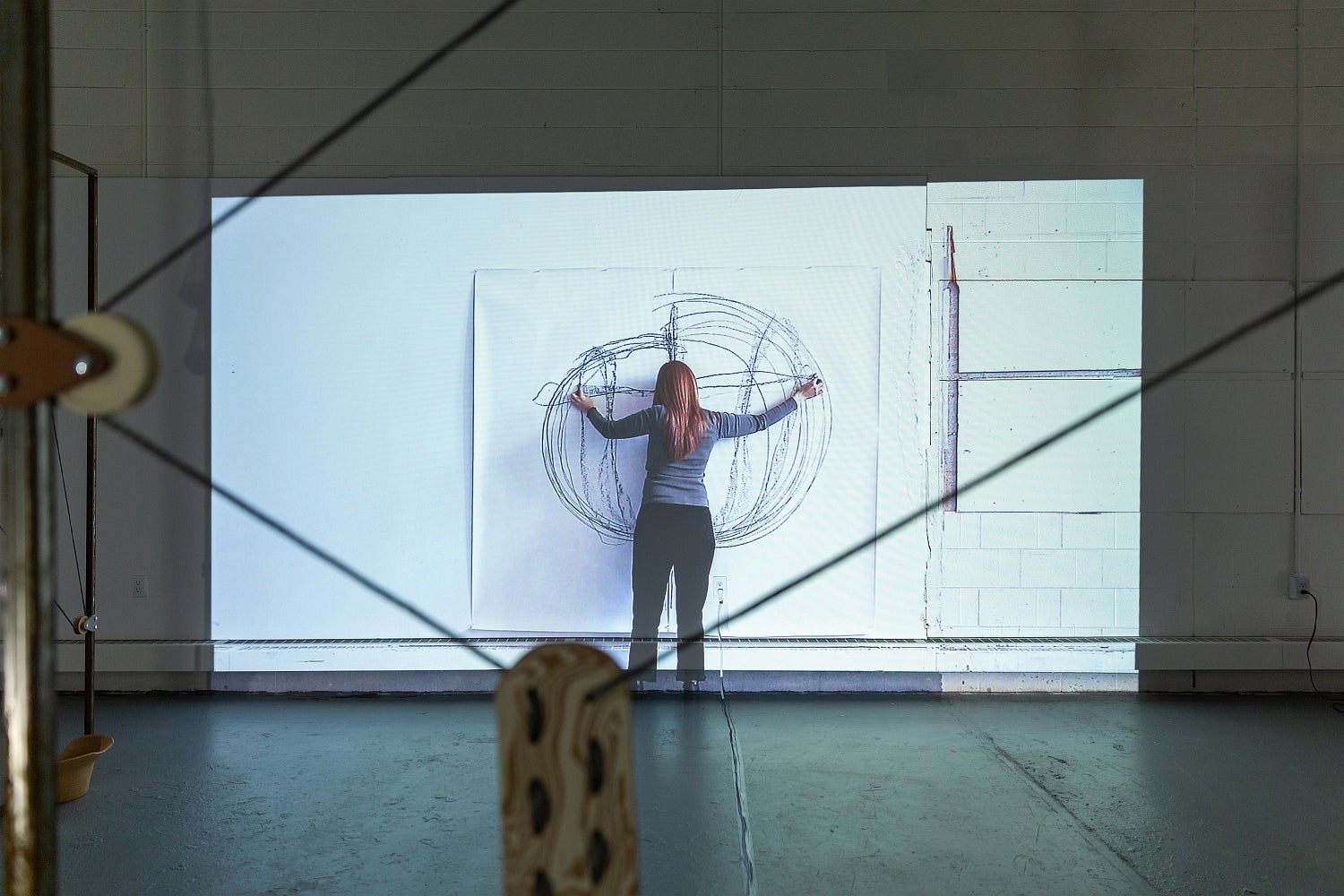 Video of a person drawing on large paper hung on a wall.  The person draws a circular shape using each arm in a sweeping motion,
