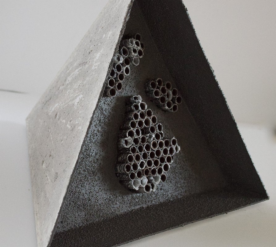 Close-up of a small pyramid form. One side is recessed with small cylinder shapes joined in rows and forming irregular shapes.