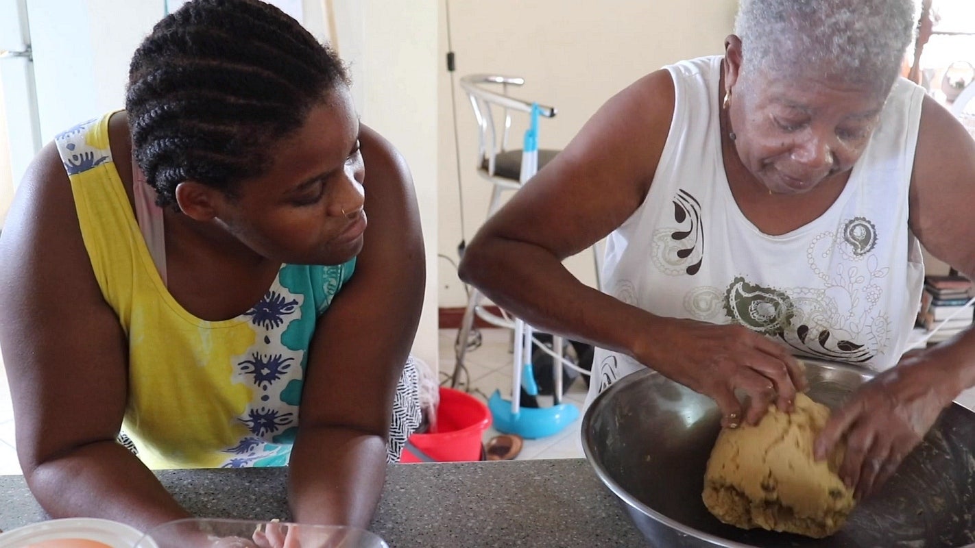 Video still, close up view of younger person watching older person mix dough with their hands