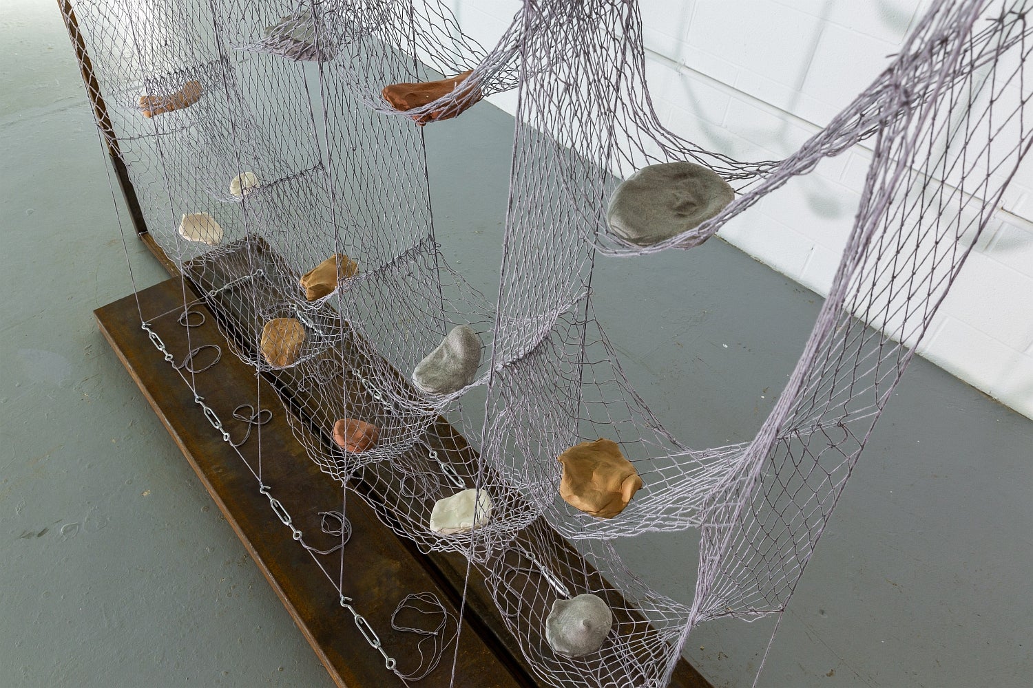 Artwork of suspended hammock-like net with sections holding rock-like ceramic objects.