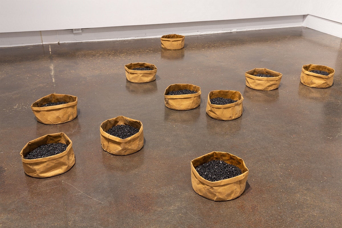 Artwork on gallery floor. A series of 10 large, circular, paper bags with the tops rolled down and filled with asphalt.