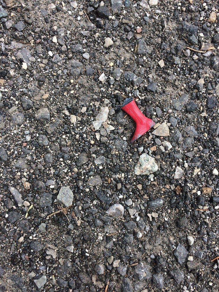 One red rainboot lies on rocky ground.