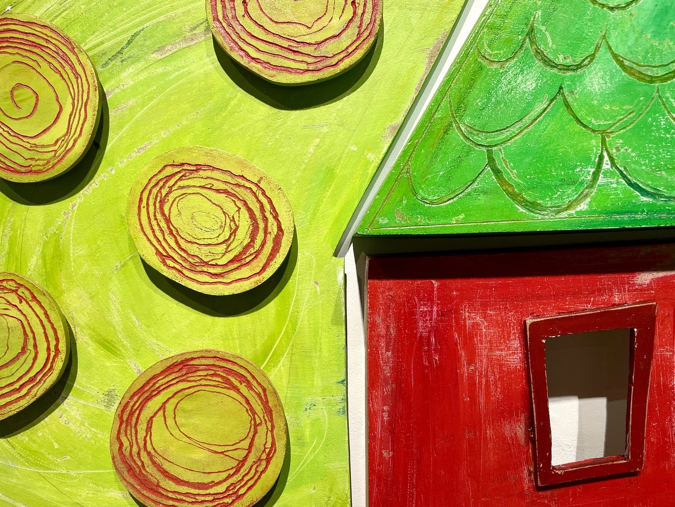Detail of artwork consisting of painted wooden shapes arranged to form a childlike red barn and tree,