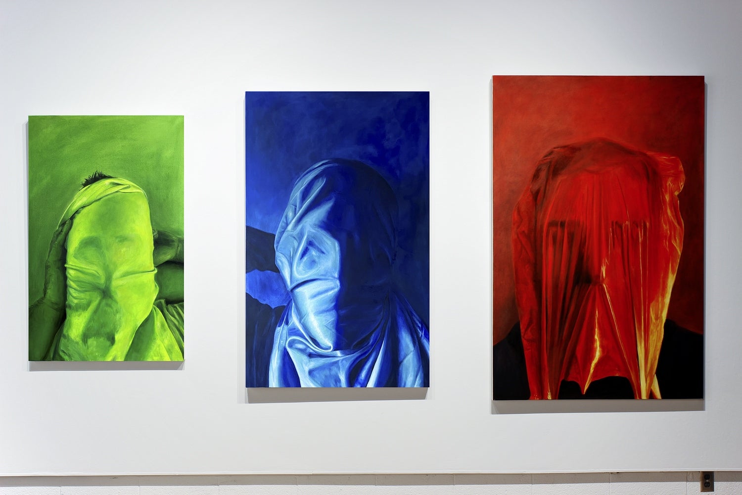 Three paintings of a head wrapped in fabric. From left to right the pictures go from smallest to largest and are coloured green,
