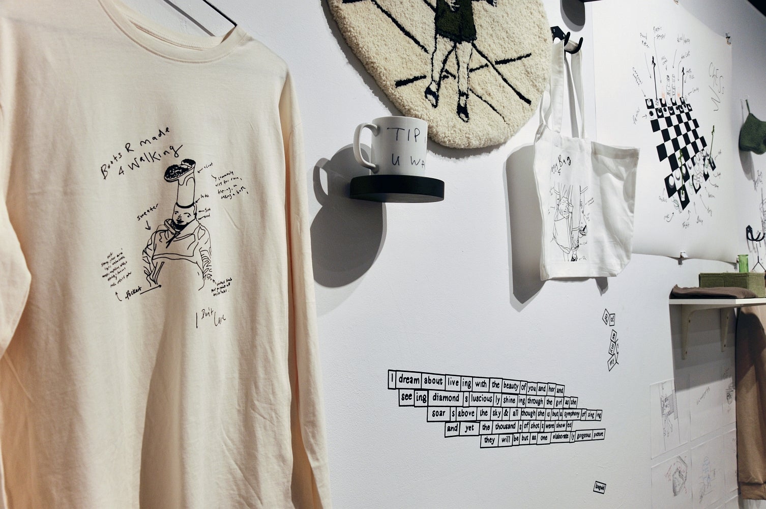 Detail of a gallery filled with various objects including sweatshirt, mug, knotted rug, pages of drawing and vinyl text.