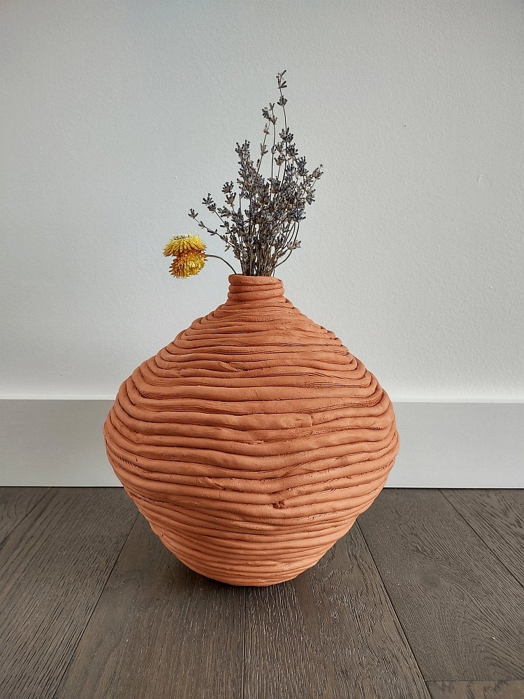 Coiled clay vessels containing dried flowers, sitting on the floor.