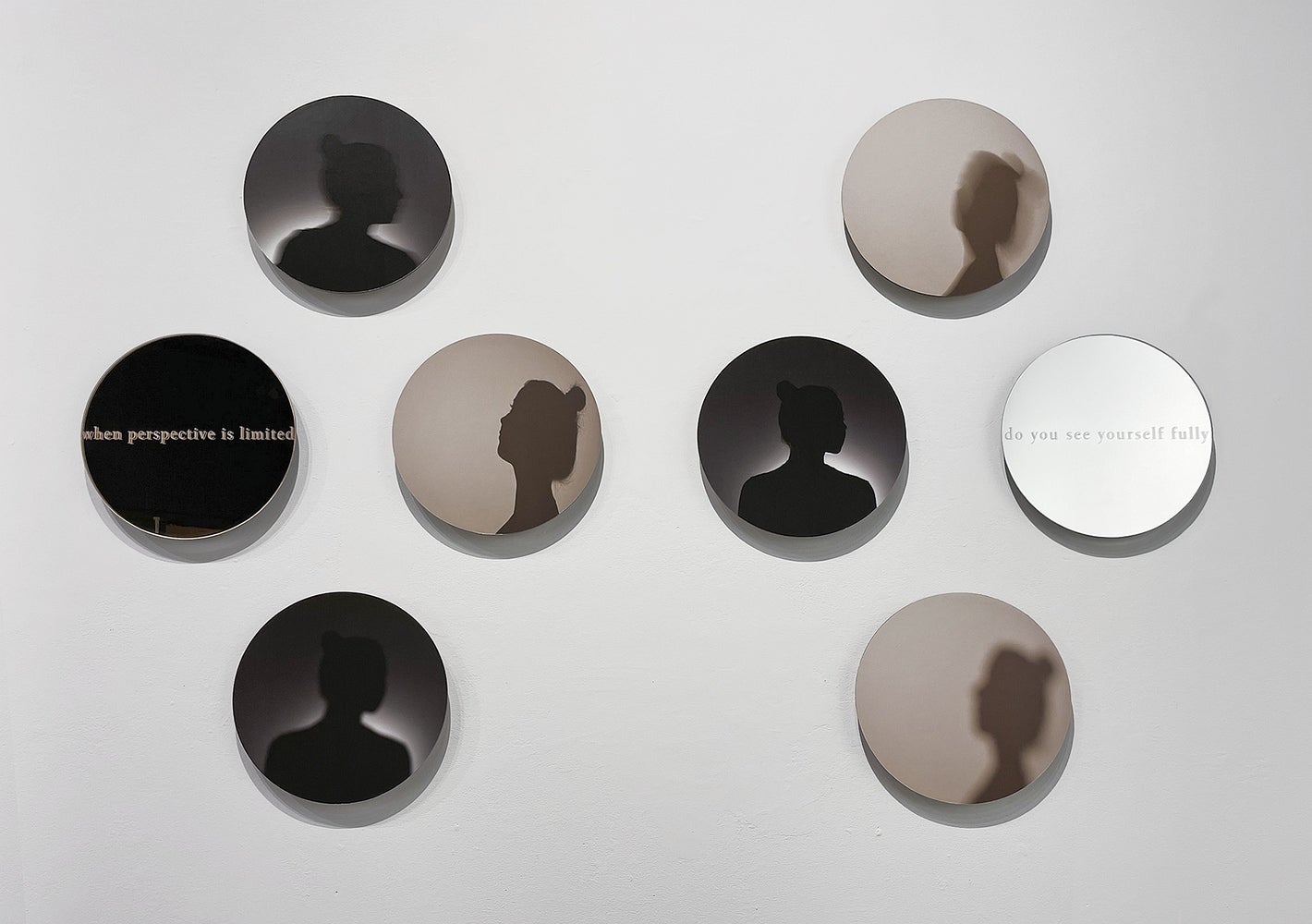 Art installation of 8 circular glass works. 6 show a woman's portrait in silhouette, 2 show text "when perspective is limited" a