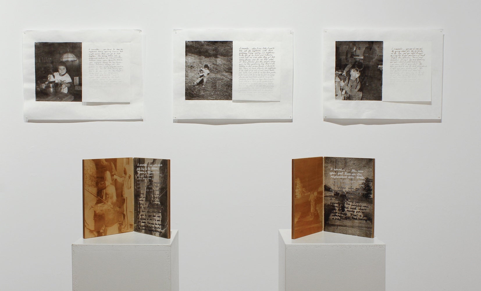 Installation in gallery of three black and white photos with accompanying text on the wall and two booklike, hinged, wooden pane