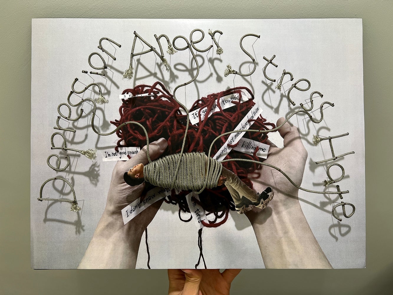 Photographic collage of two hands holding bundle of yarn with a wrapped figure, yarn forms words "depression anger stress hate"